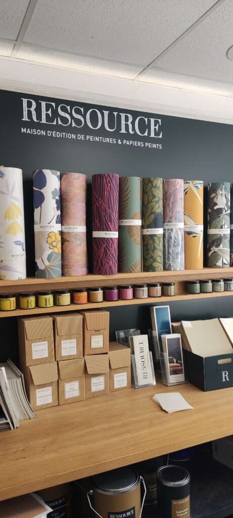 Présentation de rouleaux de papier peint de la marque Ressource, alignés sur une étagère en bois avec des motifs variés botaniques, géométriques, colorés