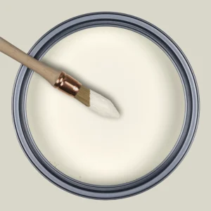 Vue de dessus d'un pot de peinture ouvert couleur blanc crème avec un pinceau à rechampir trempé dans la peinture.